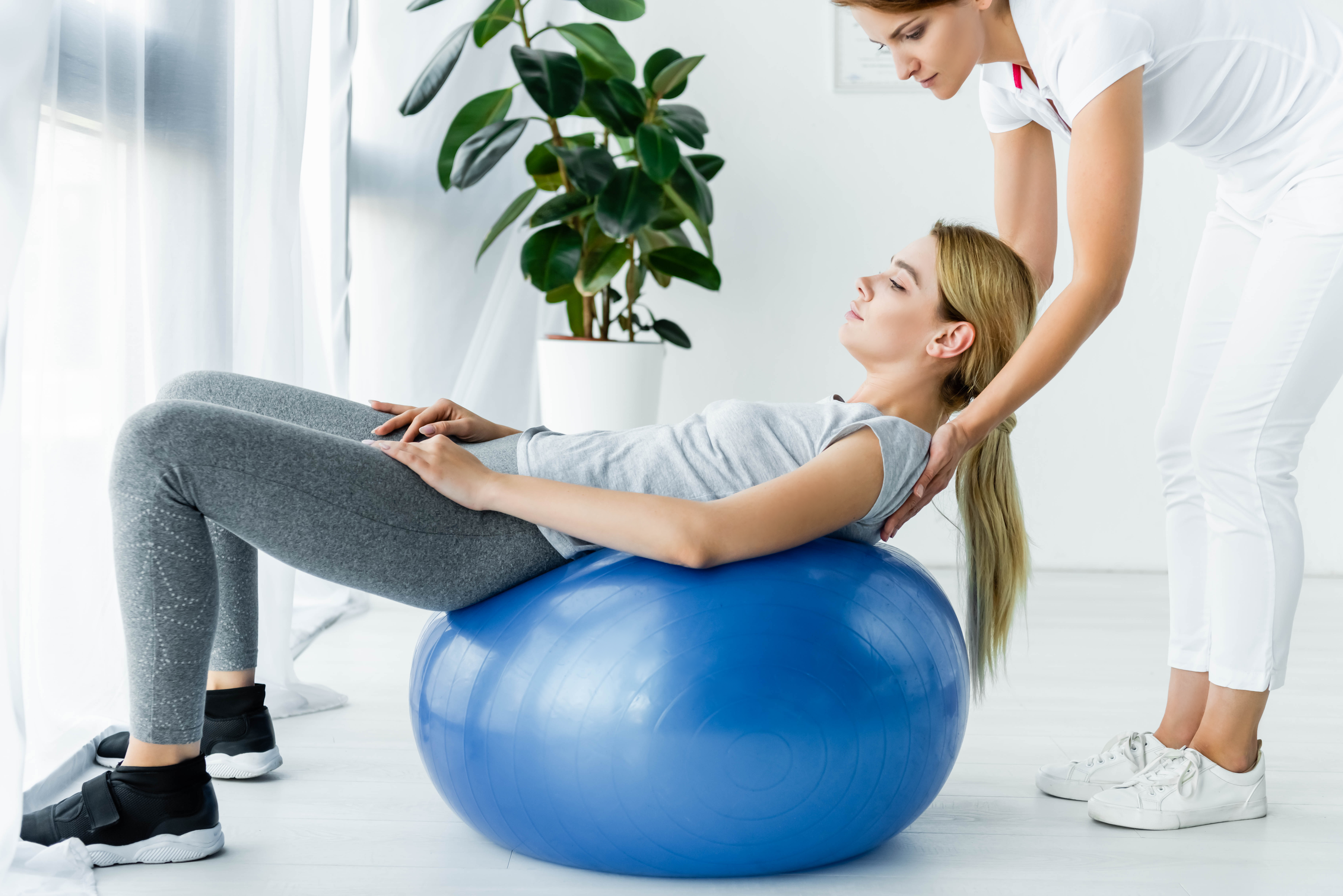 woman on an exercise ball being helped by a therapist